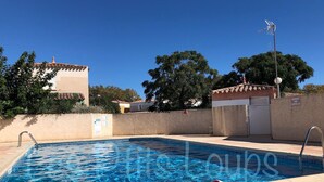 Una piscina con una torre de salvavidas, un cartel que indica una zona sin vigilancia y un cielo azul despejado.