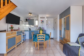 A compact kitchen with a dining area, wooden cabinets, a TV, and a staircase.
