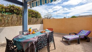 Un patio al aire libre con una mesa preparada para el desayuno, una silla de lounge y un toldo a rayas.