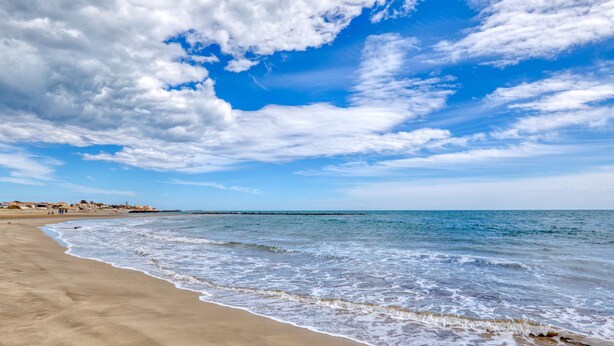 Una playa con olas, cielo despejado y edificios a lo lejos.