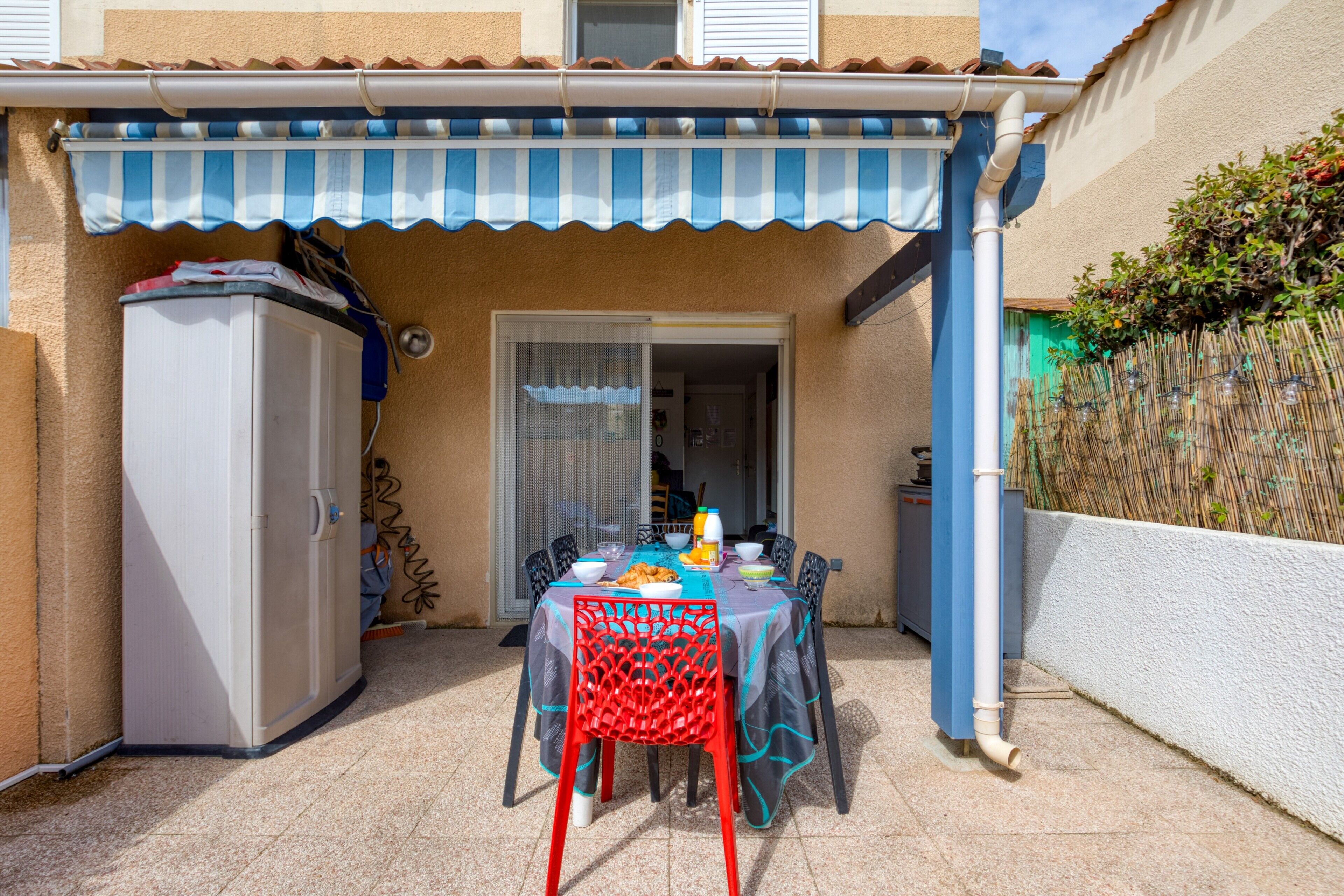 A patio with a table set for dining, a refrigerator, and a covered seating area.