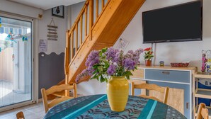 Un comedor con una mesa, sillas, un florero con flores, un televisor y una escalera.