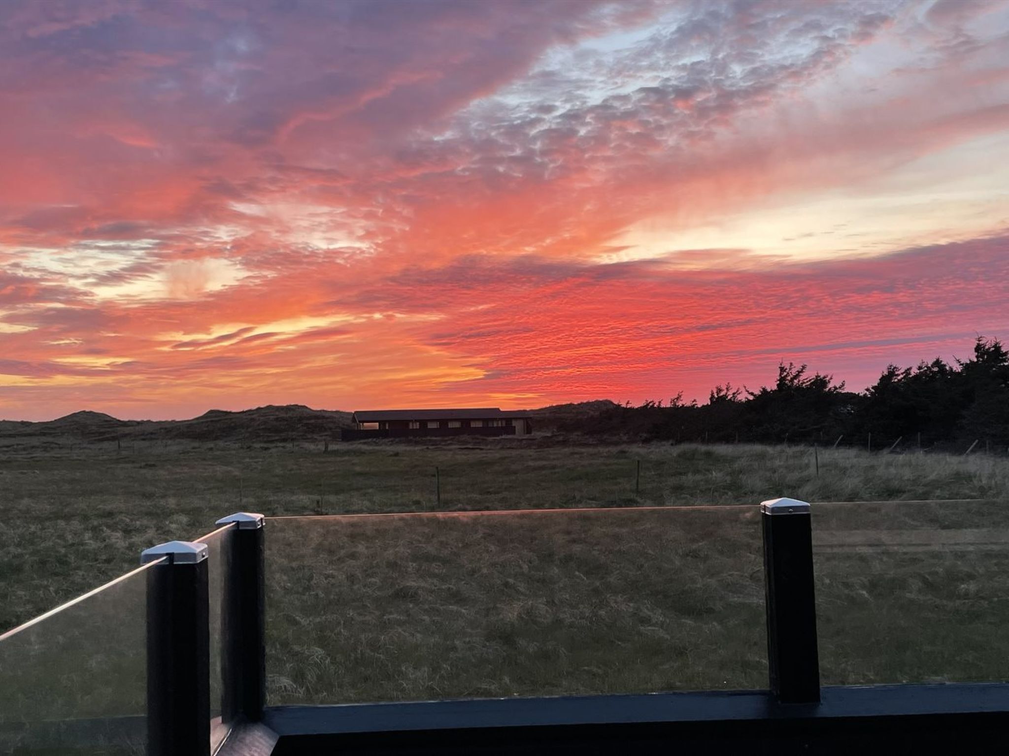 A sunset over a flat landscape with a building in the distance.