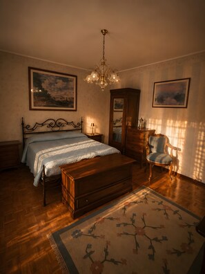 Un dormitorio con cama, un cofre de madera, una silla, cómoda y dos cuadros en la pared.