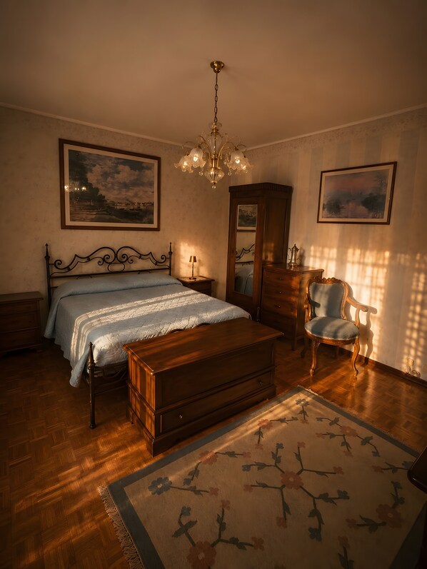 Un dormitorio con cama, un cofre de madera, una silla, cómoda y dos cuadros en la pared.