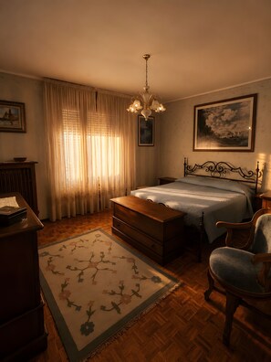 Un dormitorio con cama, una silla, un escritorio, un aparador, una araña y cortinas.