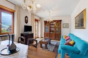 Una sala de estar con televisor, muebles de madera, una estantería y vista al mar.