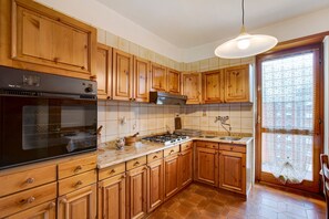 A kitchen with wooden cabinets, a stove, an oven, and a window with a curtain. - Holiday Apartment "Aosta Family Home" with Mountain View and Balcony (AOSTA)