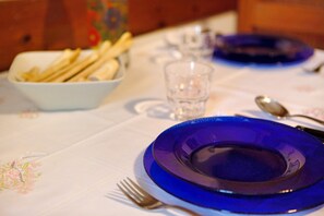 A table set with a blue plate, a bowl of breadsticks, a glass of water, and cutlery.