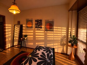 Una habitación con piso de madera, un sofá estampado con motivos florales en blanco y negro, una lámpara de pie y cuadros en la pared.