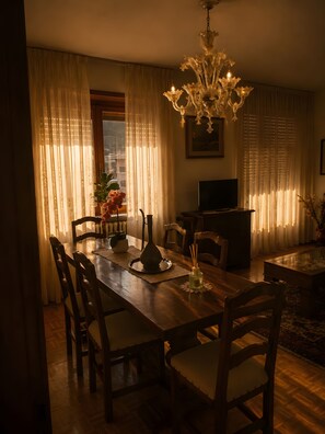 Un comedor con mesa de madera, sillas, una lámpara de araña y un televisor.