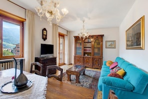 A living room with a television, wooden furniture, a chandelier, a sofa, and a view of mountains. - Holiday Apartment "Aosta Family Home" with Mountain View and Balcony (AOSTA)