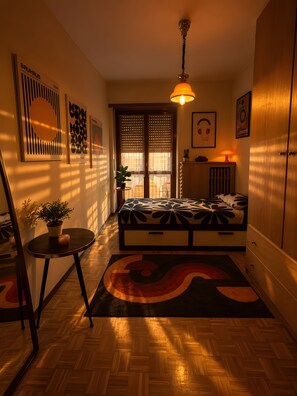 Una habitación con una cama, una mesita con una planta, un radiador y una ventana con persianas.