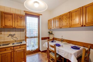 A kitchen with wooden cabinets, a sink, a dining table with chairs, and a window with a view. - Holiday Apartment "Aosta Family Home" with Mountain View and Balcony (AOSTA)