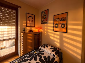A bedroom with a bed, a radiator, a window with blinds, and wall art.