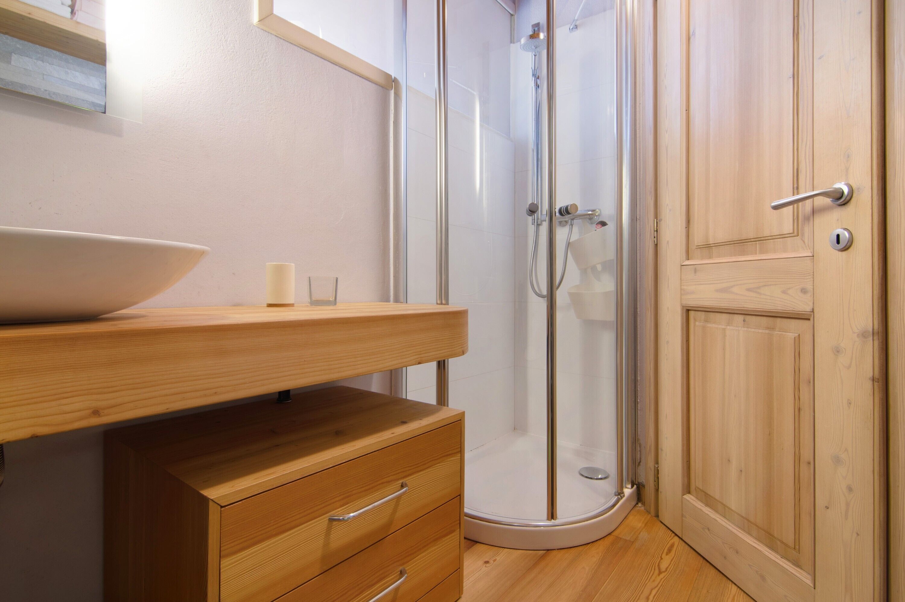 A bathroom with a wooden vanity, a glass shower enclosure, and a wooden door.
