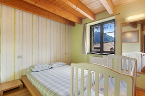 Una habitación con una cama, una cuna, un ventanal con vistas a montañas y vigas de madera en el techo.