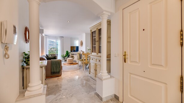 A hallway with white columns, a marble floor, a dining area with a table and chairs, and a door with a brass handle. - Apartment 'Señorio De Aloha In Puerto Banus' with Mountain View, Wi-Fi and Air Conditioning (Nueva Andalucia Marbella)