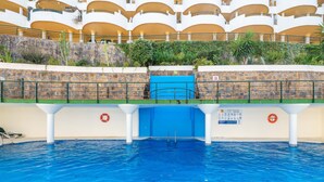 An indoor swimming pool with a diving platform, stone walls, and a view of a multi-story building with balconies. - Apartment 'Señorio De Aloha In Puerto Banus' with Mountain View, Wi-Fi and Air Conditioning (Nueva Andalucia Marbella)