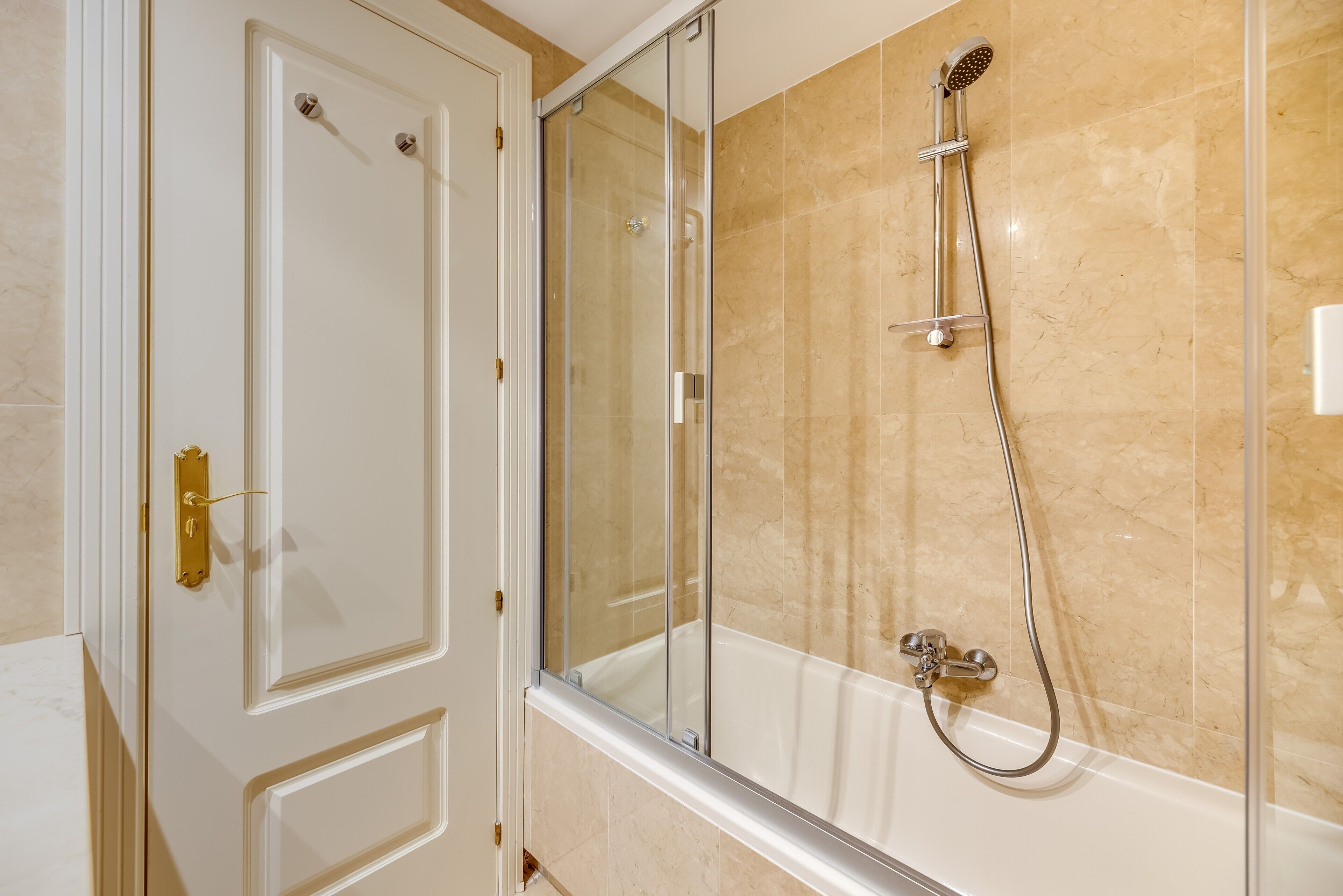 A bathroom with a glass shower enclosure, a bathtub, and a white door with a gold handle.