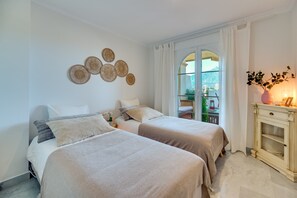 Een slaapkamer met twee bedden, een decoratieve wandversiering, een raam met gordijnen, en een nachtkastje met een vaas.