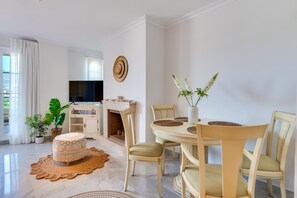 Een eethoek met een ronde tafel, stoelen en een televisie op de achtergrond.