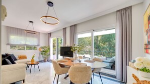 A modern living room with a dining area, large windows, and a flat-screen TV. - Apartment 'Señorio De Gonzaga In Marbella' with Shared Pool, Wi-Fi and Air Conditioning (Marbella)
