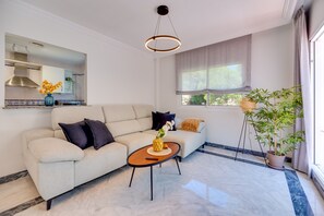 Uma sala de estar moderna com sofá, mesa de centro, planta pendente e janela com cortinas.