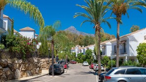 A street lined with parked cars, palm trees, and white buildings with red-tiled roofs. - Apartment 'Señorio De Gonzaga In Marbella' with Shared Pool, Wi-Fi and Air Conditioning (Marbella)