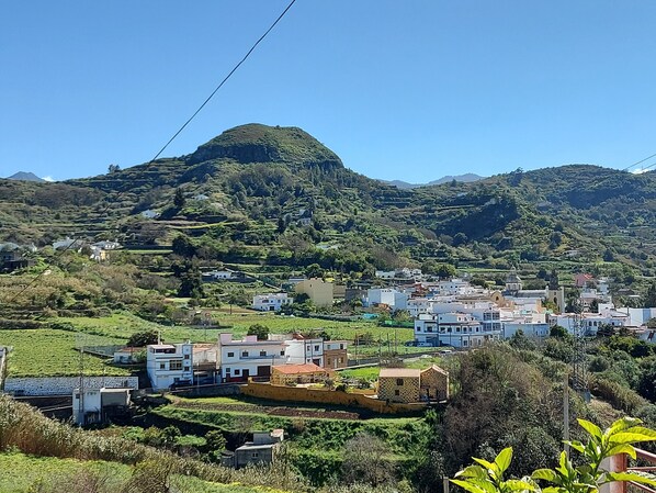 A hillside village with buildings, a prominent hill, and lush greenery.
