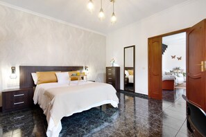 Ein Schlafzimmer mit Bett, Nachttischen, einem Schminktisch und einem Spiegel, sowie einer Tür zu einem anderen Raum.