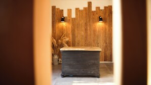 Een houten wand met twee zwarte wandlampen, een donker houten bankje en een vaas met gedroogde planten.