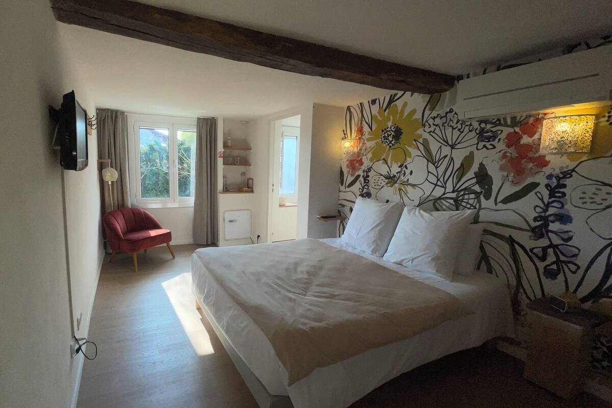 Une chambre avec un lit, une chaise, une télévision et un mur décoré de motifs floraux.