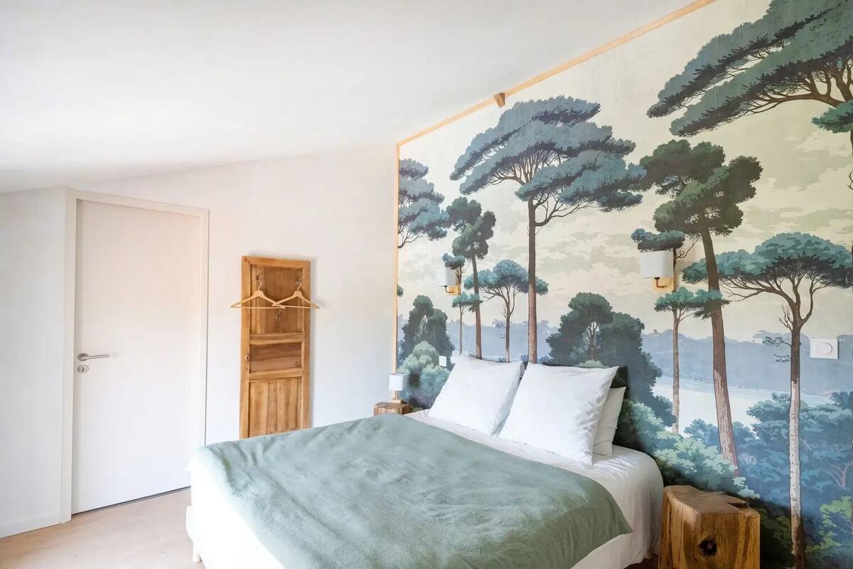 Une chambre à coucher avec un lit, une armoire en bois et une fresque représentant des arbres sur le mur.