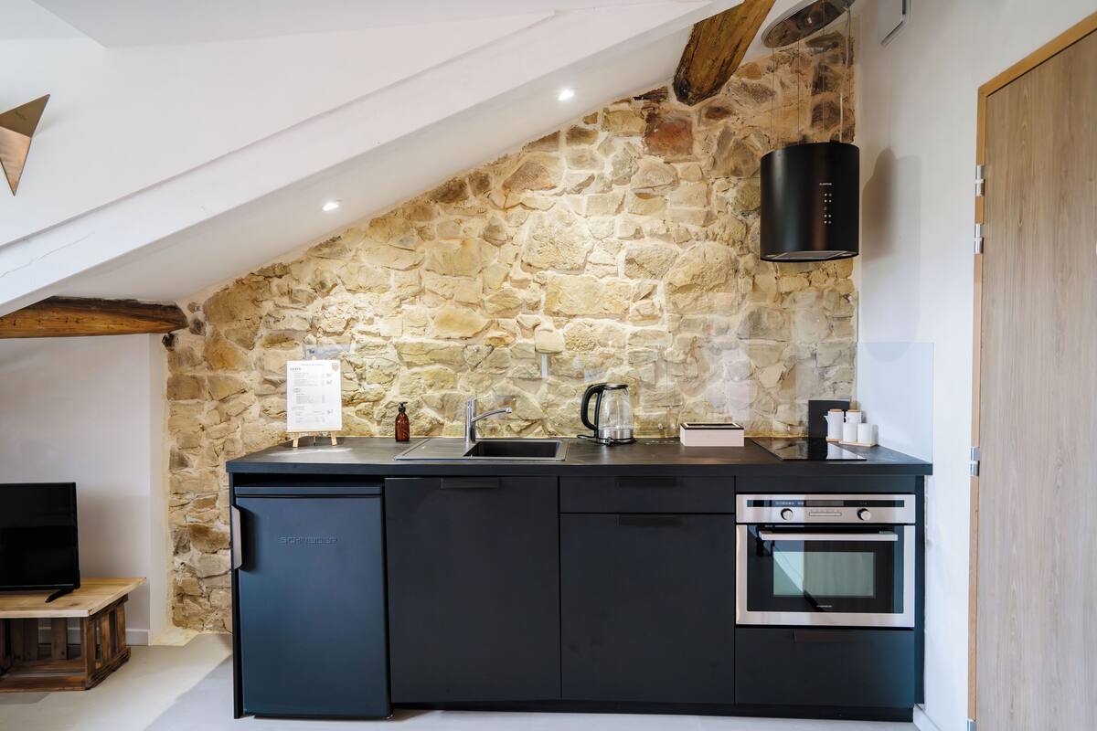 Une cuisine moderne avec un mur en pierre, des appareils électroménagers intégrés et un plafond avec une poutre en bois.