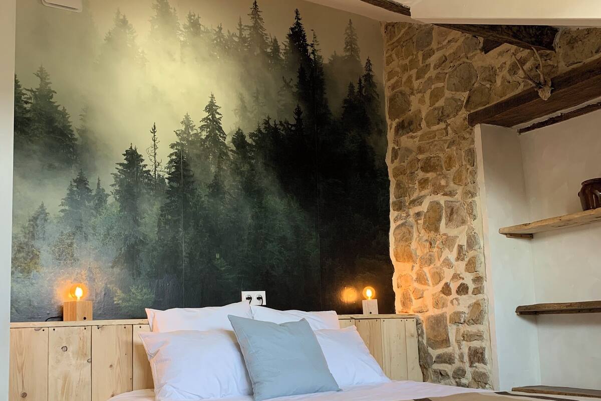 Une chambre avec un lit, un mur en pierre et une fresque représentant une forêt.