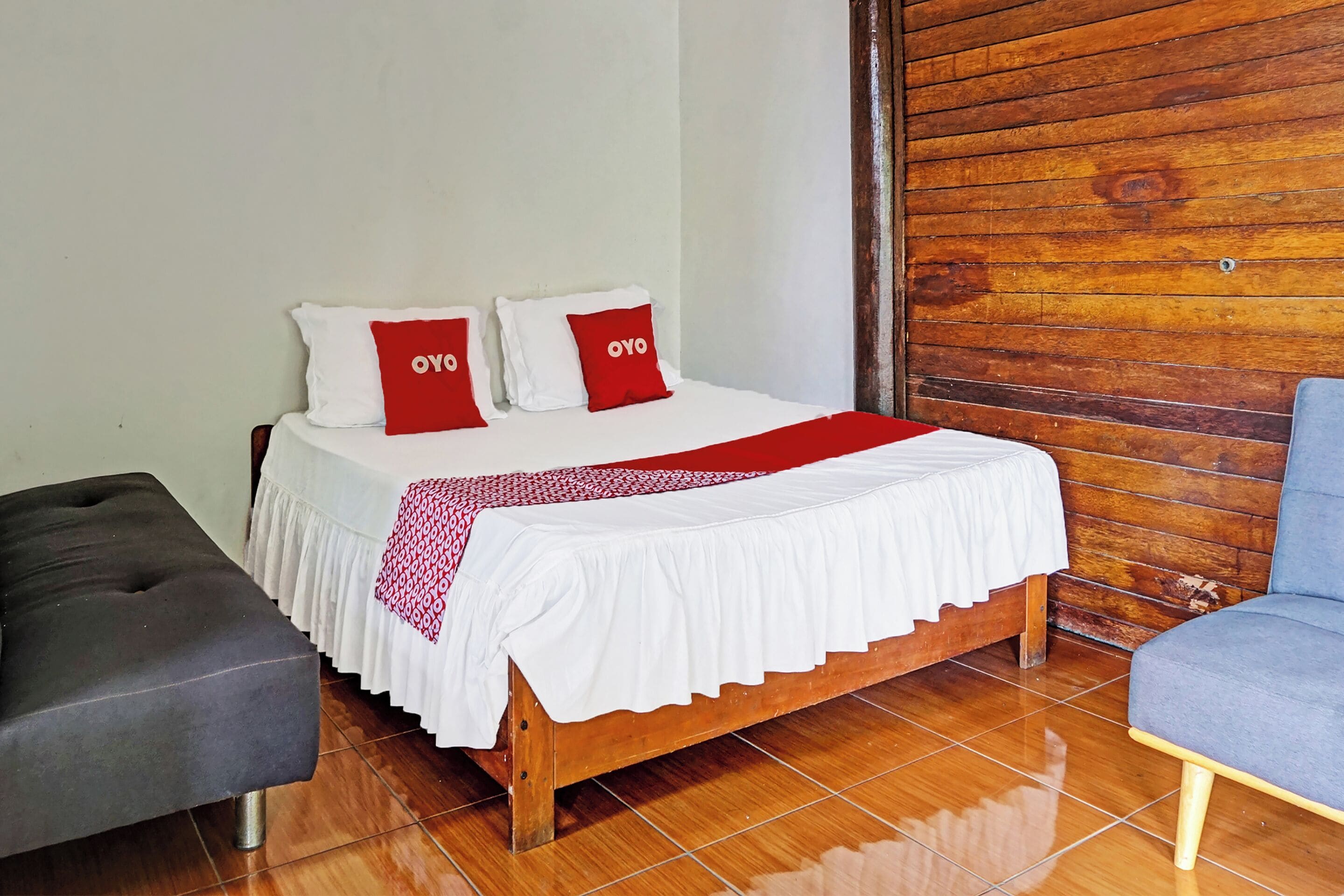 Una cama bien hecha con una colcha blanca y roja, dos almohadas con detalles rojos y un cabecero de madera.
