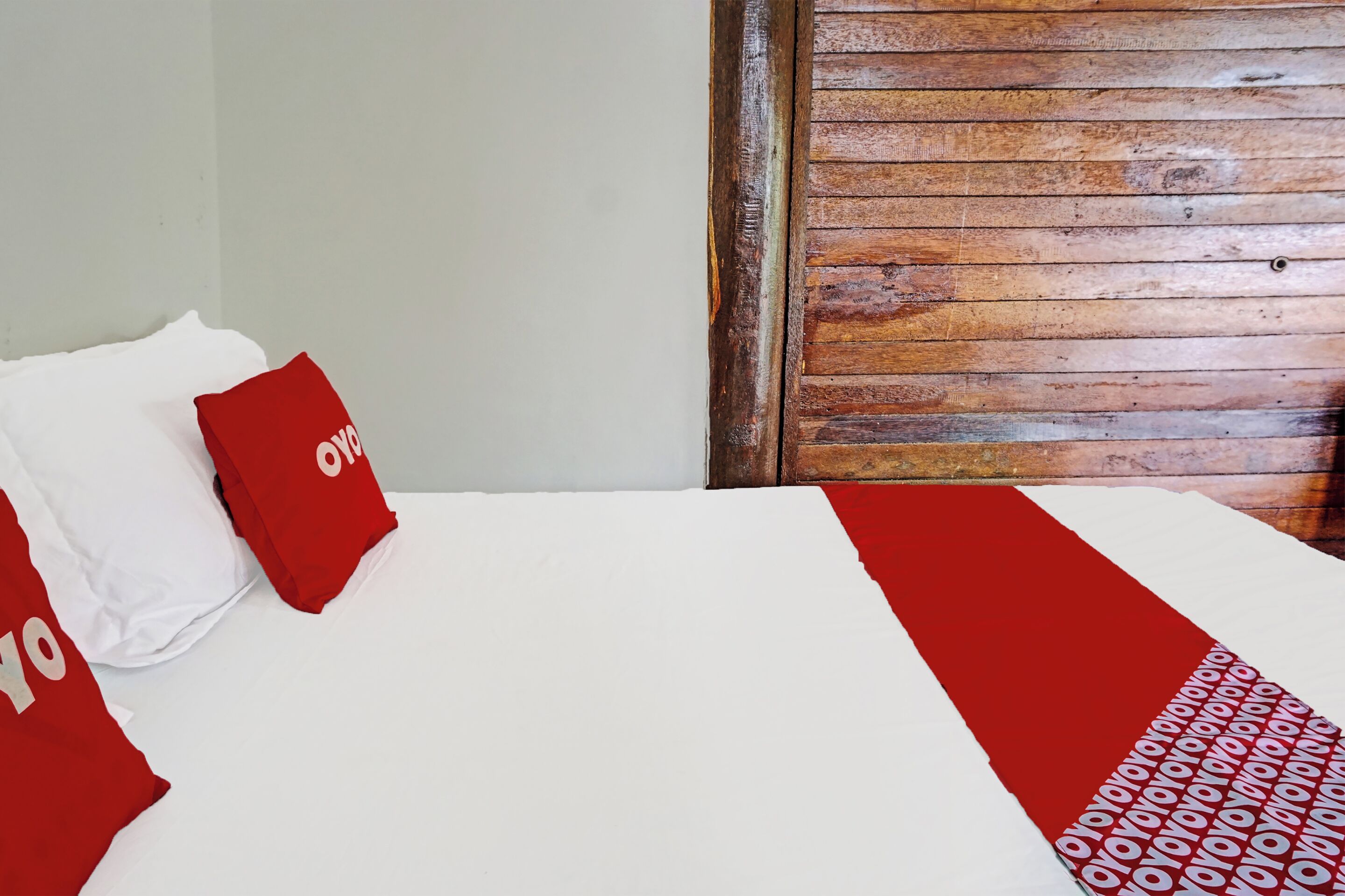 A bed with white and red bedding, a wooden headboard, and a red pillow with the word "OYO" on it.