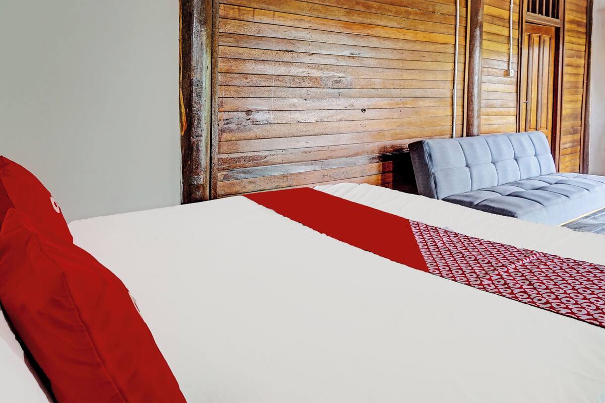 Ein Hotelzimmer mit einer Holzwand, einem Bett mit rot-weißer Bettdecke und einem grauen, gepolsterten Kopfteil.