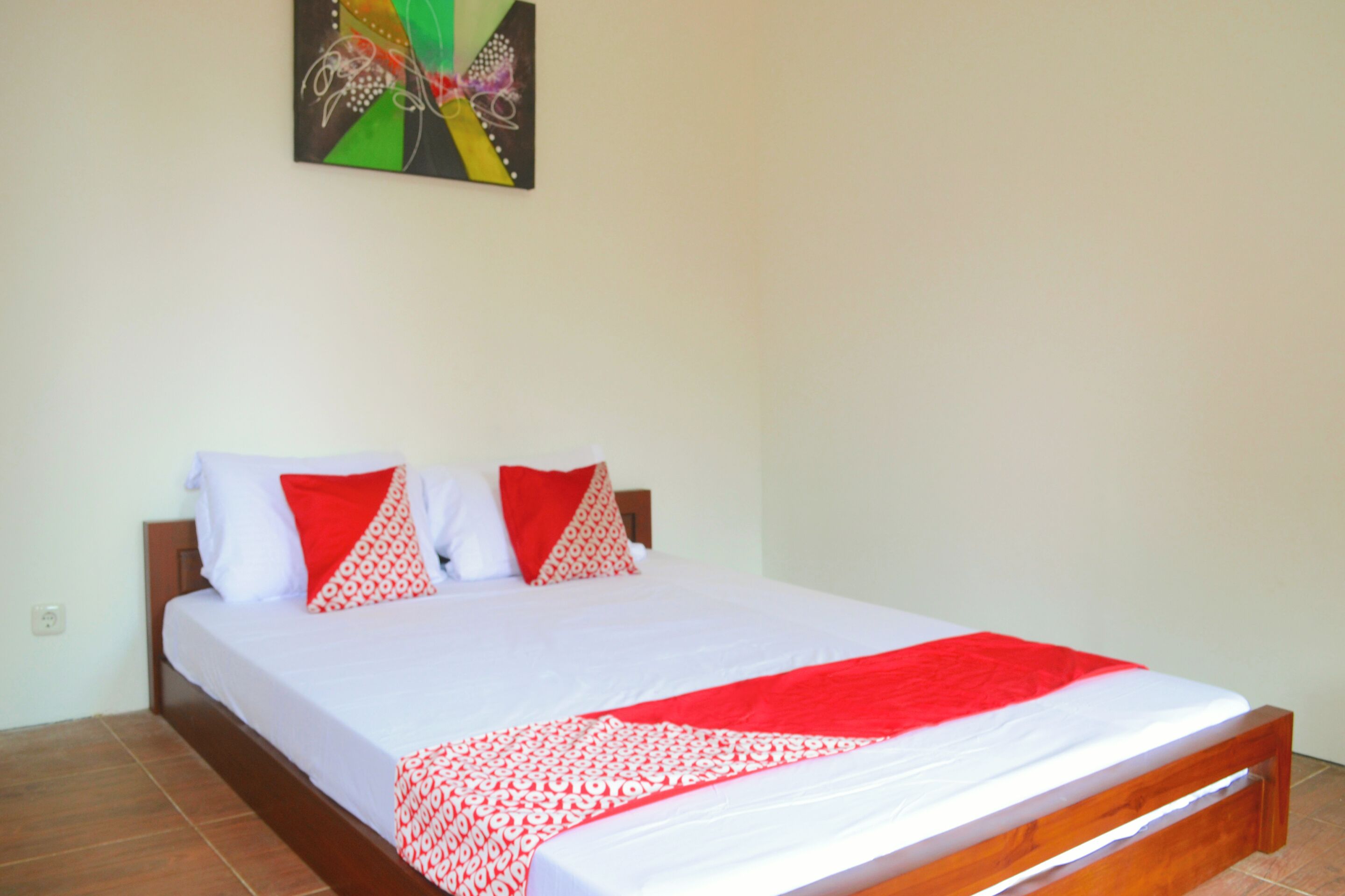 A neatly made bed with a white and red bedspread, two pillows, and a red throw blanket.