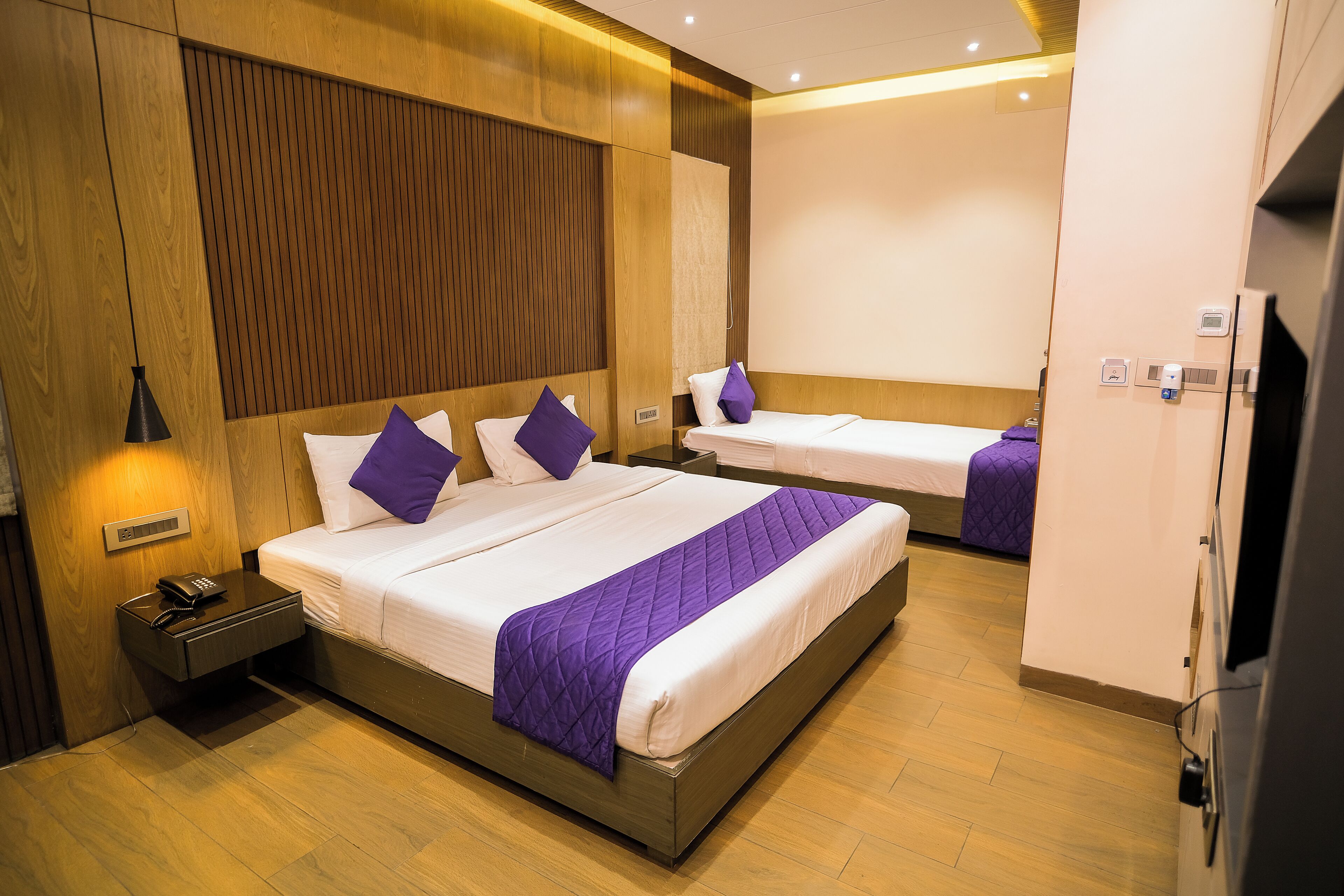 A hotel room with two beds, a wooden panel wall, a bedside table with a phone, and a TV.