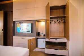 A compact hotel room with a bed, a small kitchenette, a TV, and a wooden wardrobe with hanging space.
