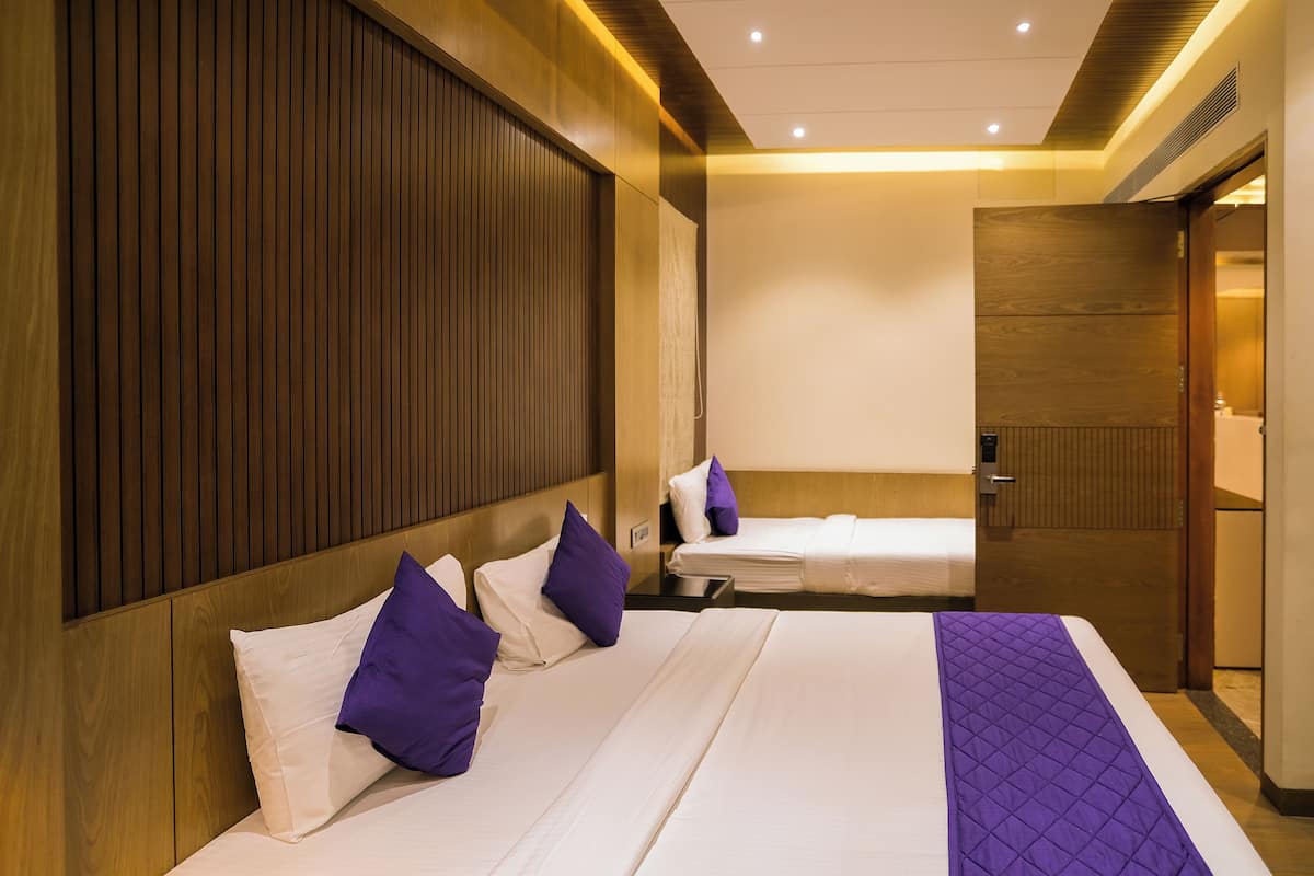 Quarto de hotel com duas camas, painéis de madeira nas paredes e porta para um banheiro.
