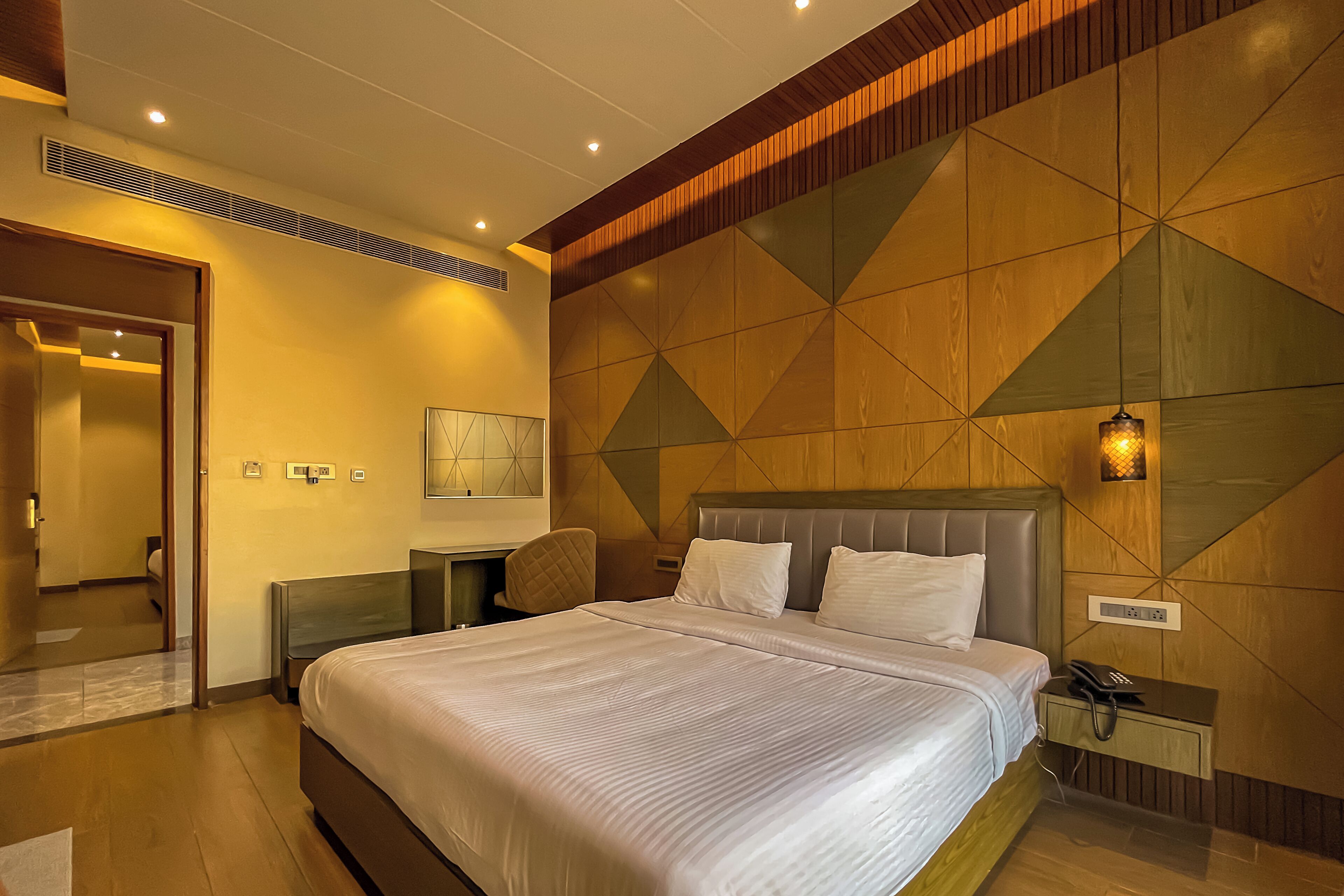 A hotel room with a large bed, a bedside table with a lamp, and a wooden accent wall.