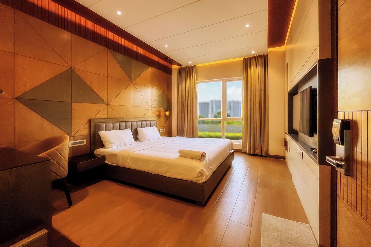 Quarto de hotel moderno com uma cama grande, televisão e vista da cidade.