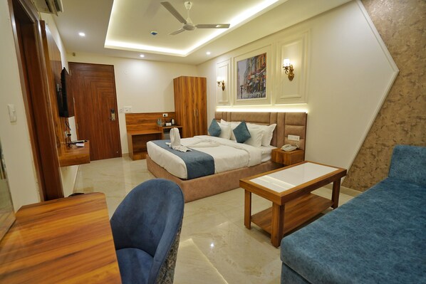 Una habitación de hotel moderna con una cama, un escritorio, una silla, un sofá, un ventilador de techo y un cuadro en la pared.