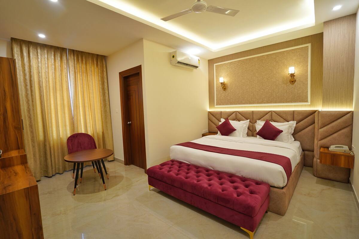 Een hotelkamer met een groot bed, een rode bekleden bank, een houten stoel, een plafondventilator en een airconditioning.