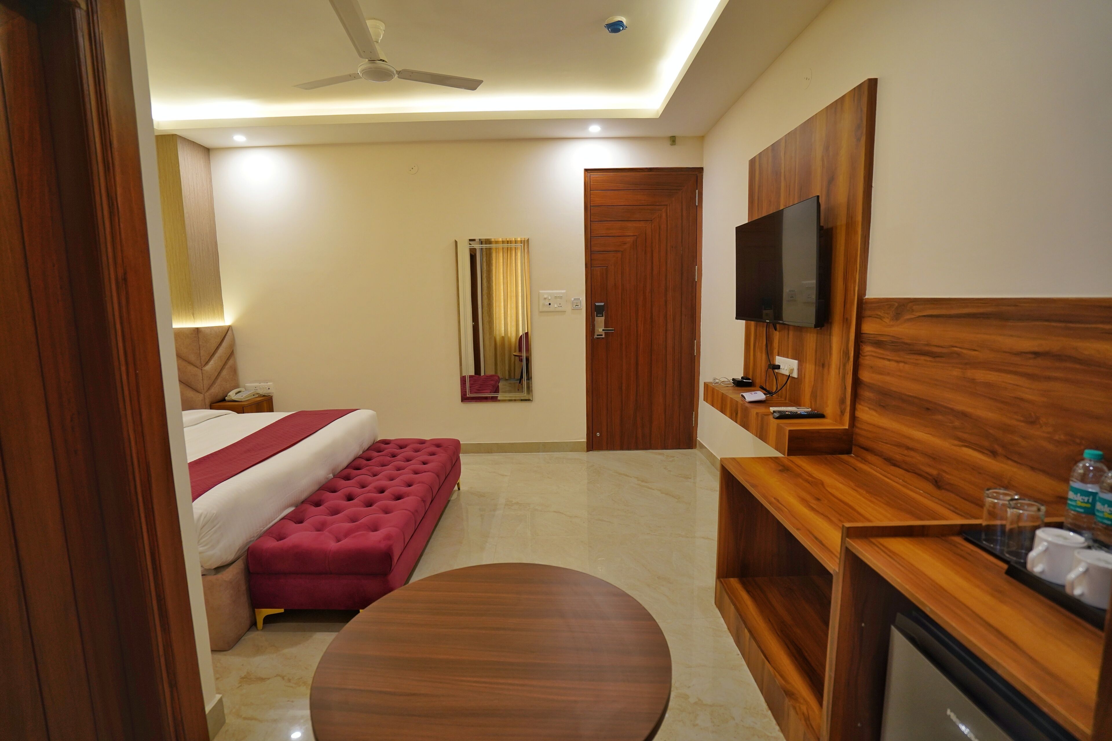 A hotel room with a bed, a TV mounted on the wall, a wooden desk, and a round table.