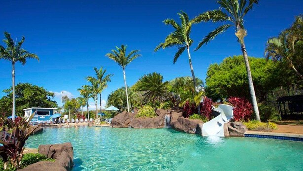 A clear pool with palm trees and rocks, a lounge area, and a waterfall feature. - Ground-Floor Retreat W/Ocean Views-Kiahuna 2166 (Koloa)