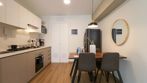 Une cuisine compacte dotée d’appareils électroménagers modernes, un coin repas avec une table et des chaises en bois, et un grand miroir au mur.